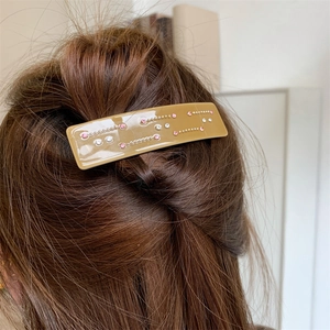 Détail d'une pince à cheveux en acétate kaki avec strass roses et perles sur cheveux