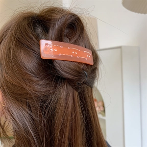 Détail d'une pince à cheveux orange translucide avec strass portée sur cheveux bruns