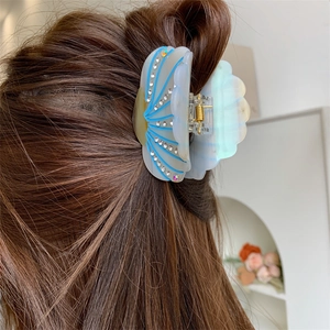 Detailed view of the shell-shaped acetate hair claw with rhinestones and blue lines