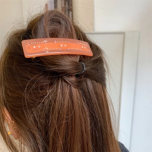 Pince à cheveux rectangulaire en résine rose orangé avec strass sur cheveux bruns