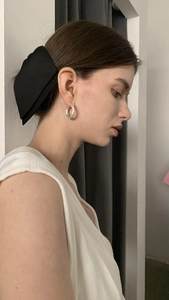 Elegant woman wearing large black satin bow hair clip and silver textured hoop earrings
