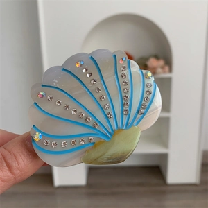 Detailed view of white shell-shaped hair claw with blue lines and inlaid crystals