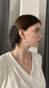 Detailed side view of an elegant black fabric bow hair clip and white textured hoop earrings