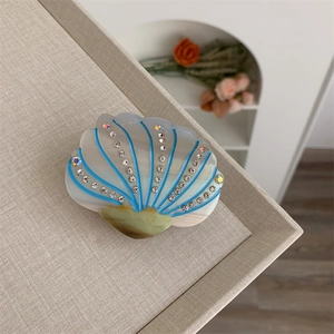 Detailed close-up of a shell-shaped acetate hair claw clip with blue stripes and rhinestones