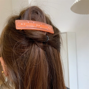 Détail d'une pince à cheveux en acétate rose avec strass portée sur des cheveux bruns