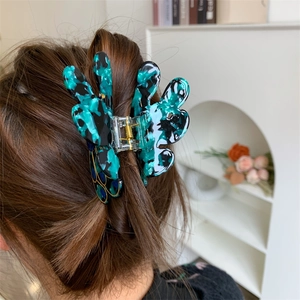 Peacock shaped acetate hair claw clip with green and black marble texture on dark hair