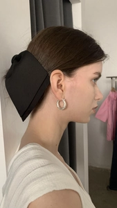 Detail of large black vintage bow hair clip and silver textured hoop earring on model
