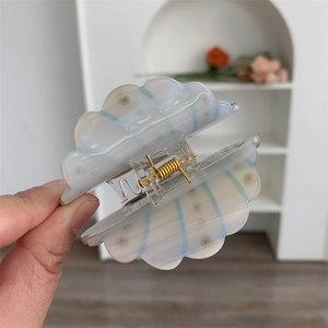 Detail shot of a shell-shaped acetate hair claw clip with blue stripes and gold spring
