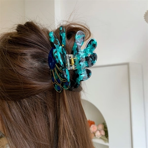 Detail of peacock pattern hair claw clip with gold metal spring on brunette hair