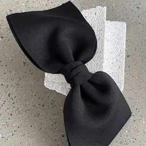 Elegant large black fabric bow hair clip displayed on a white decorative stone base