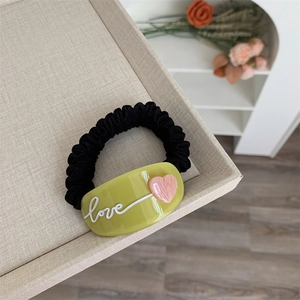Détail d'un chouchou noir avec breloque acrylique vert olive love et cœur rose doux