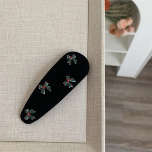 Detail view of black velvet BB hair clip featuring festive red and green plaid bows