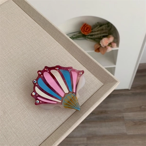 Detail view of a seashell-shaped acetate hair claw clip with colorful rhinestones inlay