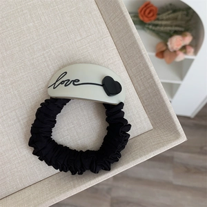 Détail du chouchou en tissu noir avec breloque LOVE beige et décor de cœur