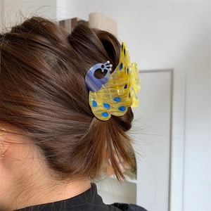 Detail of peacock hair claw clip in colorful acetate worn on a bun hairstyle