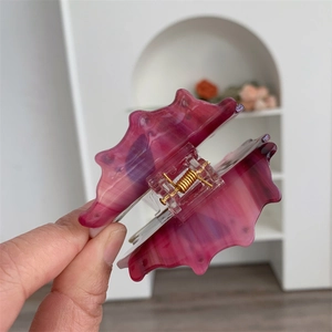 Detail of shell-shaped acetate hair claw clip with dark pink marble texture and gold spring