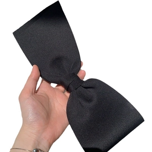 Elegant large black satin bow hair clip held in hand against a clean white background