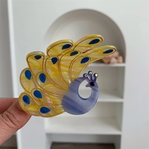 Macro detail of peacock hair claw clip featuring yellow marble patterns and blue crystal accents