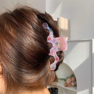 Détail d'une pince à cheveux en résine marbrée rose avec motif de fleurs en strass