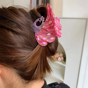 Close-up of peacock-shaped hair claw in pink and purple resin with golden accents