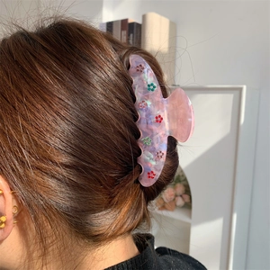 Détail de la pince à cheveux en acétate rose avec fleurs en strass colorés portée