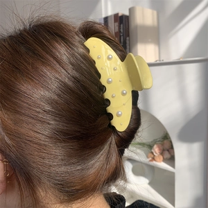 Dettaglio molletta gialla con perle bianche sui capelli in ambiente accogliente