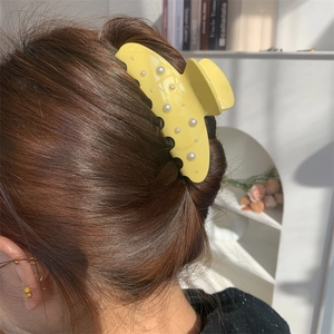 Elegante pinza per capelli in acetato giallo con perle indossata su lunghi capelli castani