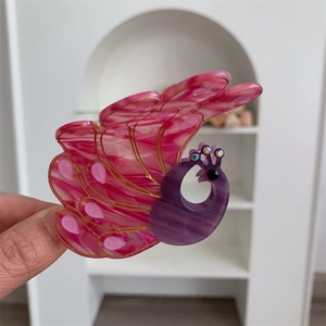 Detailed macro view of peacock hair claw clip with pink marble texture and gold accents