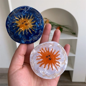 Detail of round acetate hair claws with marble texture and sun face design in blue and white