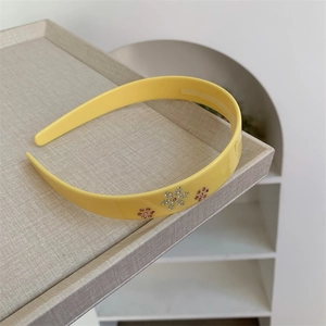 Dettaglio di cerchietto giallo in acetato con fiori di strass e denti antiscivolo