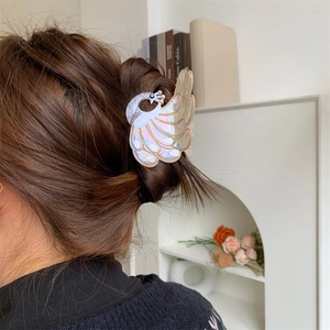 Detailed view of a white peacock hair claw clip with pearlescent finish on dark brown hair
