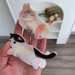 Dettaglio ravvicinato delle pinze per capelli a forma di gatto con texture perlata e linee oro