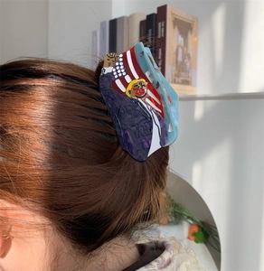 Dettaglio di un grande fermaglio per capelli in acetato con design Trump