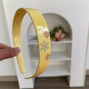 Dettaglio di un cerchietto giallo in acetato con delicati fiori di strass rosa e bianchi