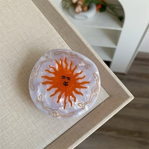 Detail of sun-shaped acetate hair claw featuring marble texture and vintage sun pattern