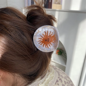 Detail of sun motif acetate hair claw with white marble pattern on model