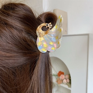 Detail view of peacock hair claw clip with pearlescent finish on dark wavy hair