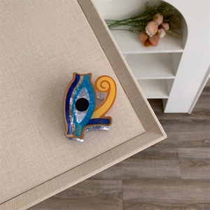 Detailed view of an artistic acrylic eye-shaped hair claw clip on a textured beige tray