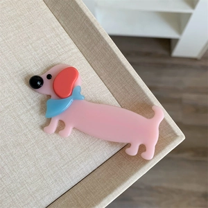 Primo piano di un fermaglio per capelli in acetato rosa a forma di cane su vassoio beige