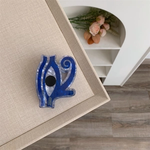Detail of blue acrylic hair claw clip with Eye of Horus pattern on a beige tray