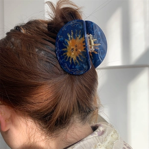 Retro blue acetate hair claw with sun face pattern worn by a model in natural sunlight