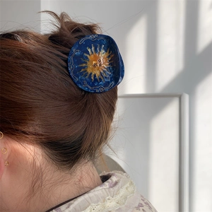Detail showing a blue acetate sun hair claw clip styled on a brown ponytail