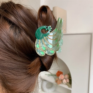 Peacock shaped hair claw with iridescent finish and gold details on brown hair