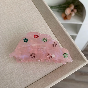 Gros plan d'une pince à cheveux fleur rose translucide avec strass colorés sur plateau