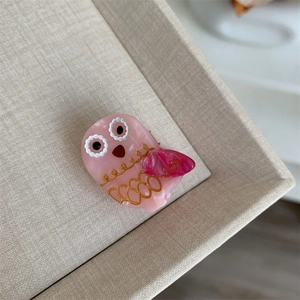Detalle de pinza para pelo de búho rosa con plumas doradas y acabado de acetato