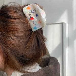 Detail van de parelmoer acetaat haarklem met Love-tekst en hartpatroon op golvend bruin haar