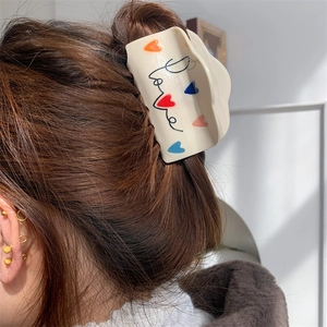 Detail van crème haarklem met Love-tekst en kleurrijke hartjes op het haar gedragen