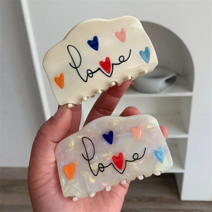 Detail van vierkante haarklemmen met hartpatronen en love-tekst getoond in de hand