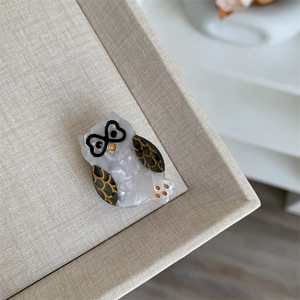 Detalle de pinza para el pelo de búho en acetato blanco con gafas de corazón y alas oro