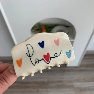 Detail van een crème haarklem van acetaat met kleurrijke hartjes en Love-tekst